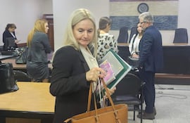 Ana Girala, con carpeta y bolso, se retira de la sala. En el fondo.