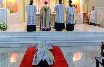 Sacerdote con túnica en misa, mientras asistentes de espaldas observan en un ambiente religioso con decoración típica.