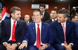Horacio Cartes y Santiago Peña sonríen en trajes oscuros, mientras Pedro Alliana escucha atentamente en ambiente formal.