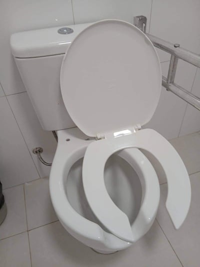 Inodoro blanco con tapa abierta en un baño, entorno limpio con azulejos blancos.