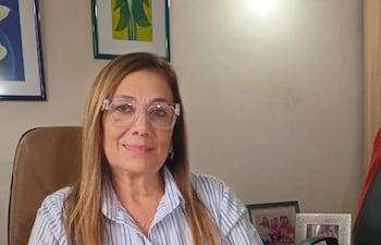 Sonia Escauriza con camisa a rayas y gafas, sentada en un escritorio rodeada de documentos, sonriendo mientras trabaja.