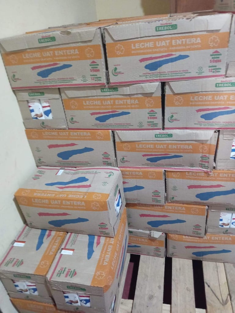 Cajas de cartón apiladas con inscripción 'Leche UAT Entera' en un depósito de madera, sin personas visibles.