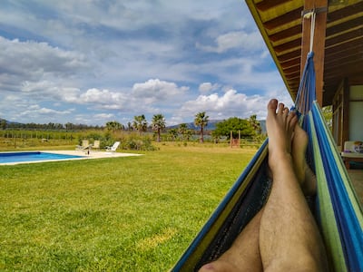 Una persona descansa con los pies descalzos en una hamaca paraguaya, en una quinta al costado de una pileta.