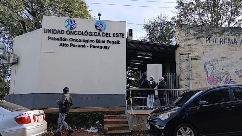 Dos mujeres con gorros conversan fuera del pabellón oncológico, un hombre escucha de pie mientras otro se aleja.