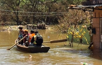 Cuatro niños en canoa; uno rema, otro viste camiseta oscura, otro tiene gorra naranja, y el cuarto lleva chaleco reflectante.