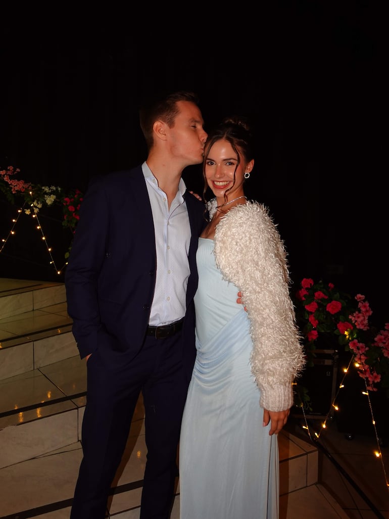 Joshua Duerksen en chaqueta oscura y Anneke Rahn en vestido azul claro, sonriendo en un entorno festivo.