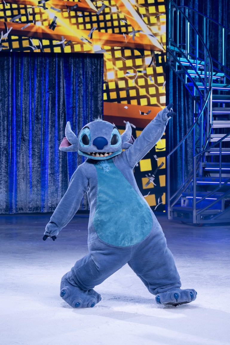 Personaje azul de Stitch en pista de hielo, con brazo levantado y fondo iluminado por luces de espectáculo.