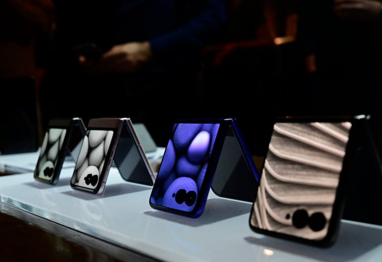 Teléfonos móviles plegables en mesa blanca, exhibidos en ambiente oscuro con luz enfocada.