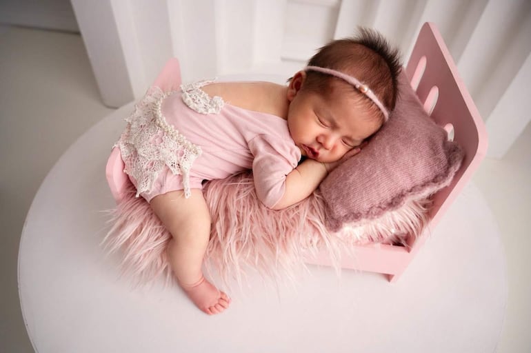 Bebé en cuna rosa con body rosa claro y diadema delgada, durmiendo con expresión tranquila en entorno suave.