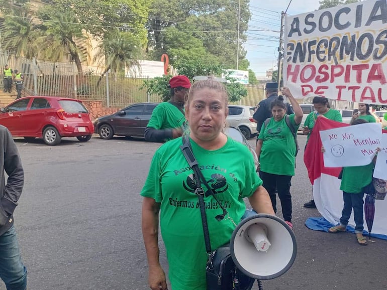 Mujer con altavoz lidera la protesta, rodeada de personas con camisetas verdes y carteles en un entorno urbano.