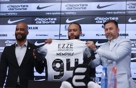 El futbolista neerlandés Memphis Depay (c), sostiene la camisa del Corinthians durante su presentación como nuevo jugador del club acompañado del presidente del Corinthians Augusto Melo (d) y el manager Fabio Soldado (i), durante una rueda de prensa este jueves en el estadio Neo Química Arena, sede del club Corinthians en Sao Paulo (Brasil). Depay fue recibido como una estrella en el aeropuerto internacional de Guarulhos, en São Paulo, por la afición del Corinthians, en un momento en que el equipo lucha por no descender a segunda división.