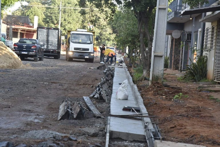 Cuatro trabajadores con chalecos naranjas y camiones en una calle en construcción de Asunción.