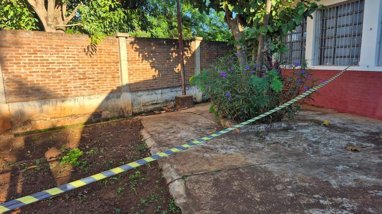 Patio de la Escuela Básica N°3770 San Miguel, con cinta de seguridad en el suelo y vegetación descuidada alrededor.