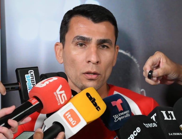 Junior Alonso vestido con camiseta roja habla a una multitud de periodistas, rodeado de micrófonos de distintos medios.