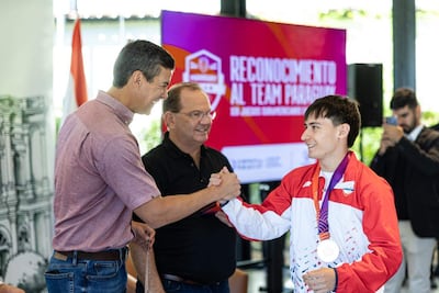 Camilo Perez Lopez Moreira y Santiago Peña sonríen durante el reconocimiento, mientras un joven con chaqueta roja sostiene una medalla.