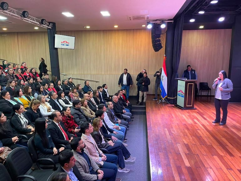 Mujer con chaqueta clara habla en el auditorio, audiencia atenta y banderas de Paraguay en el fondo.