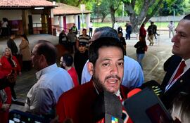 Raúl Latorre con chaqueta roja rodeado de micrófonos, mientras habla a una multitud en un entorno al aire libre.