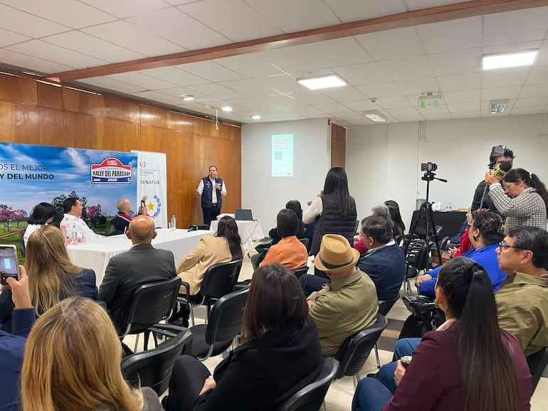 Jacinto Santa María en chaqueta presenta la Guía Turística del Rally, rodeado de asistentes que toman notas en un entorno formal.