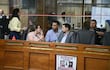 Luis Fernando Bernal en blusa amarilla habla en recinto legislativo, mientras Pablo Callizo escucha atentamente con gesto serio.