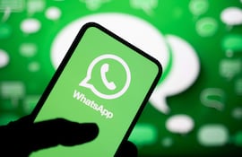 Teléfono móvil con el logotipo verde y blanco de WhatsApp, sostenido por una mano en un fondo borroso verde.