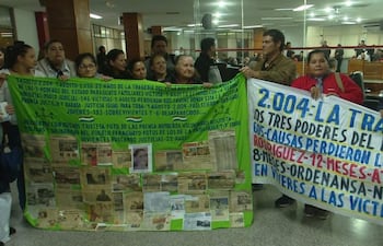 Grupo de personas sosteniendo pancartas en un edificio público, expresiones serias en un ambiente de protesta pacífica.