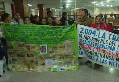 Grupo de personas sosteniendo pancartas en un edificio público, expresiones serias en un ambiente de protesta pacífica.