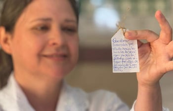 Mujer de cabello castaño y blusa blanca sostiene una etiqueta con un mensaje emotivo en un entorno acogedor.