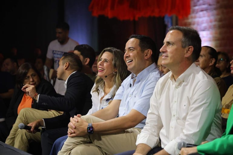 Soledad Núñez sonríe entre Ricardo Estigarribia, en chaqueta negra, y Kattya González, en blusa blanca, en un evento iluminado.