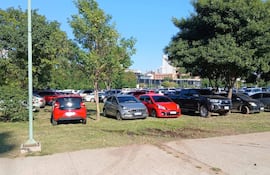 Varios vehículos estacionados en césped de la Plaza España, rodeados de árboles y bajo un cielo despejado.