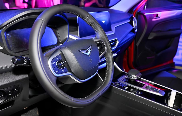 Interior de automóvil moderno con volante y panel de control iluminados en tonos azules y morados.