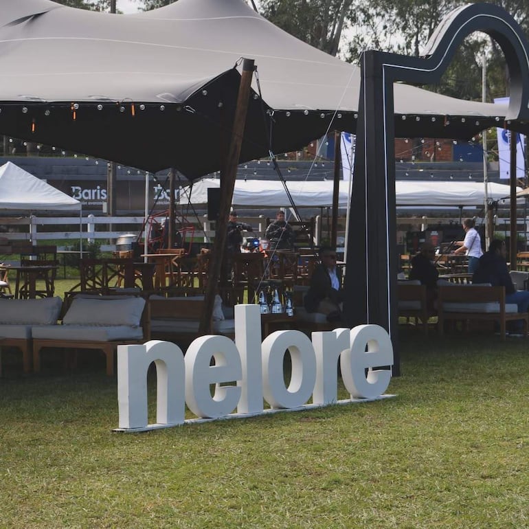 Letrero grande que dice 'nelore' en un ambiente al aire libre, con carpas y mesas listas para recibir a los visitantes.