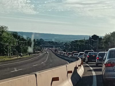 Carretera saturada con vehículos en fila, bajo un cielo parcialmente nublado en un día soleado.