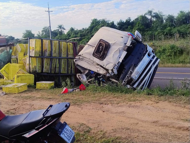Camión volcado en la carretera, rodeado de cajas amarillas vacías y vegetación al fondo.