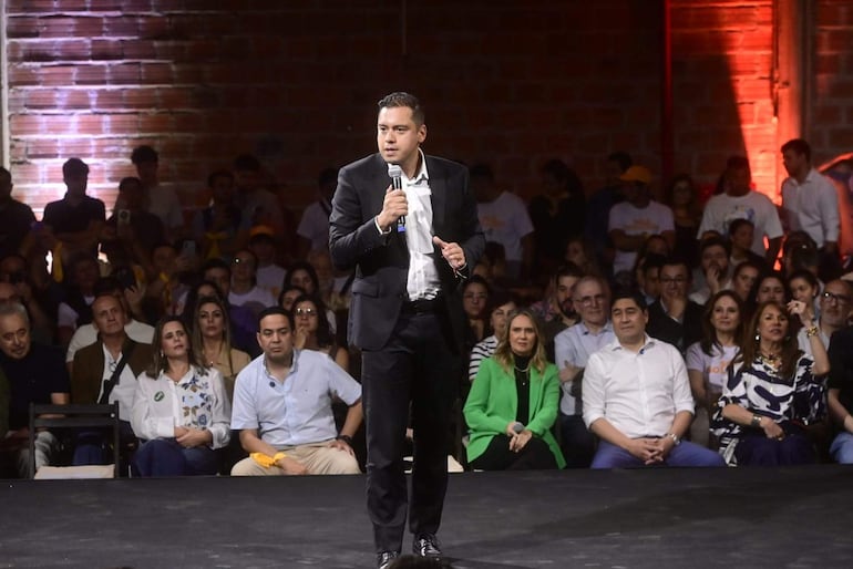 Miguel Prieto en traje negro y camisa blanca habla en el escenario, mientras la audiencia lo escucha con atención.