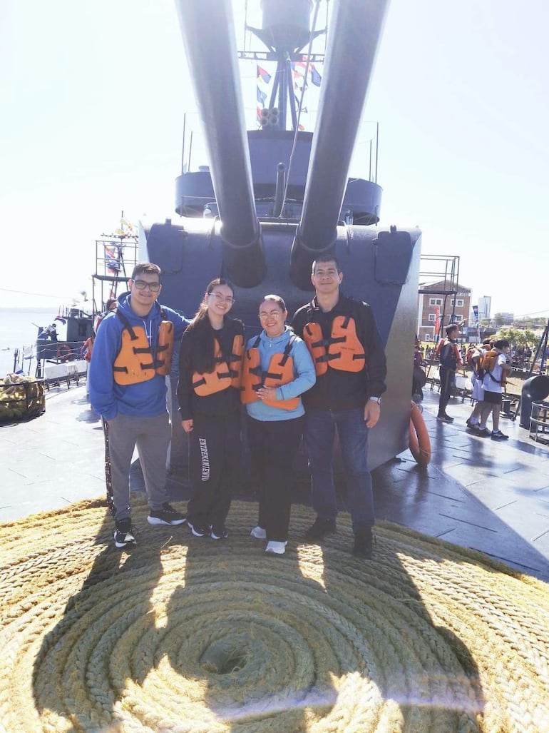 Cuatro personas sonrientes en chalecos salvavidas junto a un cañón naval, en un ambiente soleado y recreativo en un barco.