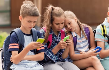 Grupo de niñas y niños sentados utilizando sus smartphones. Foto: Qustodio.
