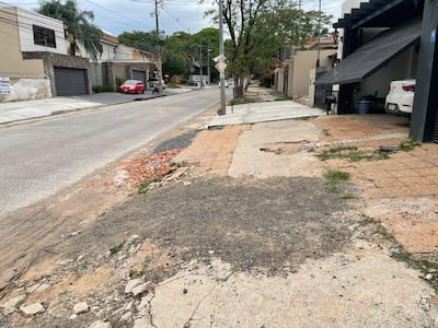 Calle urbana con calzada irregular y automóvil rojo estacionado; el ambiente es residencial y nublado.
