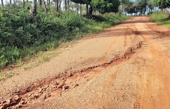 Camino de tierra deteriorado, con surcos y piedras, rodeado de vegetación abundante en una zona rural.
