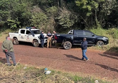 Cuatro personas, tres policías en uniforme y un civil, junto a camionetas en un camino rural con vegetación densa.