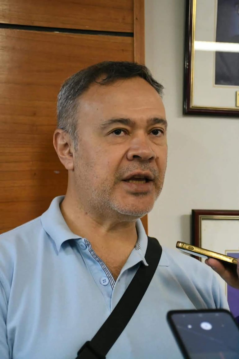 Humberto Blasco habla en un ambiente interior, vestido con camiseta celeste y bolso negro, rodeado de personas que lo graban.