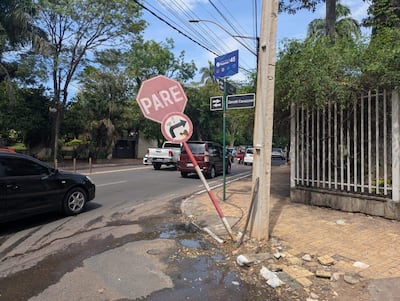 Letrero de stop inclinado en la calle, con vehículos en movimiento y un charco de agua en la acera.
