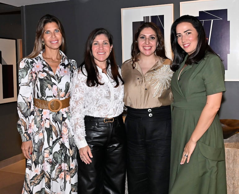 Cuatro mujeres sonrientes, una en vestido floral, otra en blusa blanca, tercera en camisa brillante y cuarta en vestido verde, en un bar moderno.