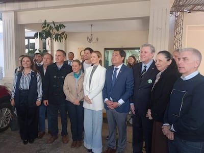 Grupo de personas sonrientes en atuendos formales, posando en un ambiente interior amigable durante un evento político.