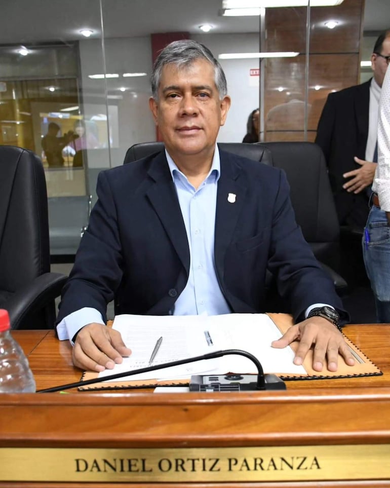Daniel Ortiz, vestido con saco oscuro y camisa clara, sentado ante documentos en un entorno institucional, con expresión serena.