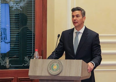 Santiago Peña en traje oscuro y corbata clara, hablando en un podio con el escudo de la República del Paraguay de fondo.