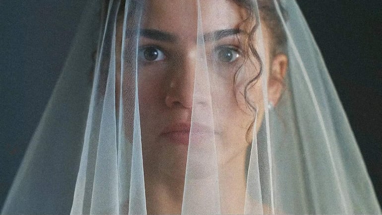 Mujer con velo y cabello oscuro, en un ambiente neutro, muestra un rostro sereno y contemplativo, sin otros individuos presentes.