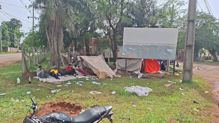 Grupo de indígenas sentados sobre el suelo en carpa blanca, algunos con camisetas de colores, en un ambiente de desamparo.