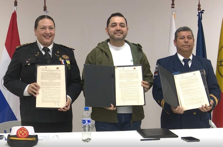 Mujer con uniforme y medallas sonríe, mientras dos hombres en uniforme sostienen documentos en un entorno oficial.