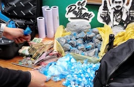 Mesa con paquetes de drogas y dinero en efectivo, rodeada de objetos que sugieren actividades ilegales. Sin personas visibles.
