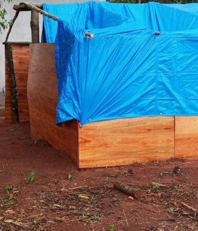 Estructura cubierta con lona azul en ambiente natural, rodeada de tierra roja y restos de vegetación cercana.